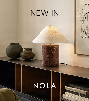 Lampă de masă Nola cu bază din marmură brun-roșcată și abajur conic din in, pe o comodă închisă la culoare. Text: „Noutate – Nola”.