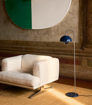 Lampă de podea elegantă &Tradition lângă un fotoliu lounge modern într-un interior primitor.