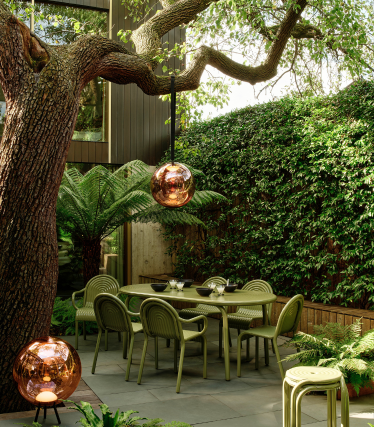 Lămpi de exterior Tom Dixon într-o grădină elegantă, cu zonă de luat masa sub un copac bătrân.