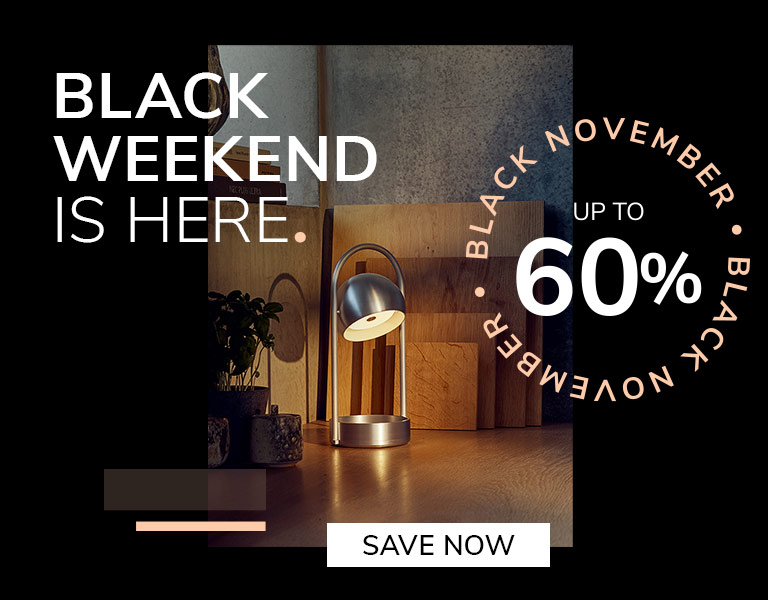 Save now “Modern silver table lamp glowing on a wooden desk with cutting boards and plants in the background. Promotional text reads: ‘Black Weekend is here. Up to 60%. Black November.’ A button says ‘Save Now.